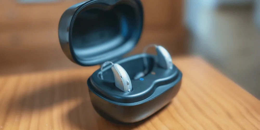 Audifono recargable en su base de carga junto a pilas desechables