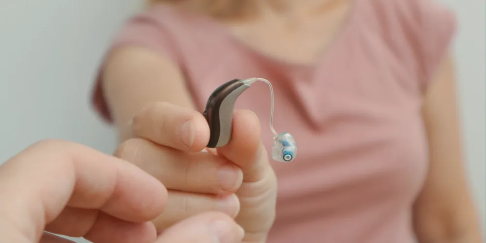 Una persona sostiene con sus dedos un audífono moderno retroauricular de diseño estilizado y pequeño en color café y plata.